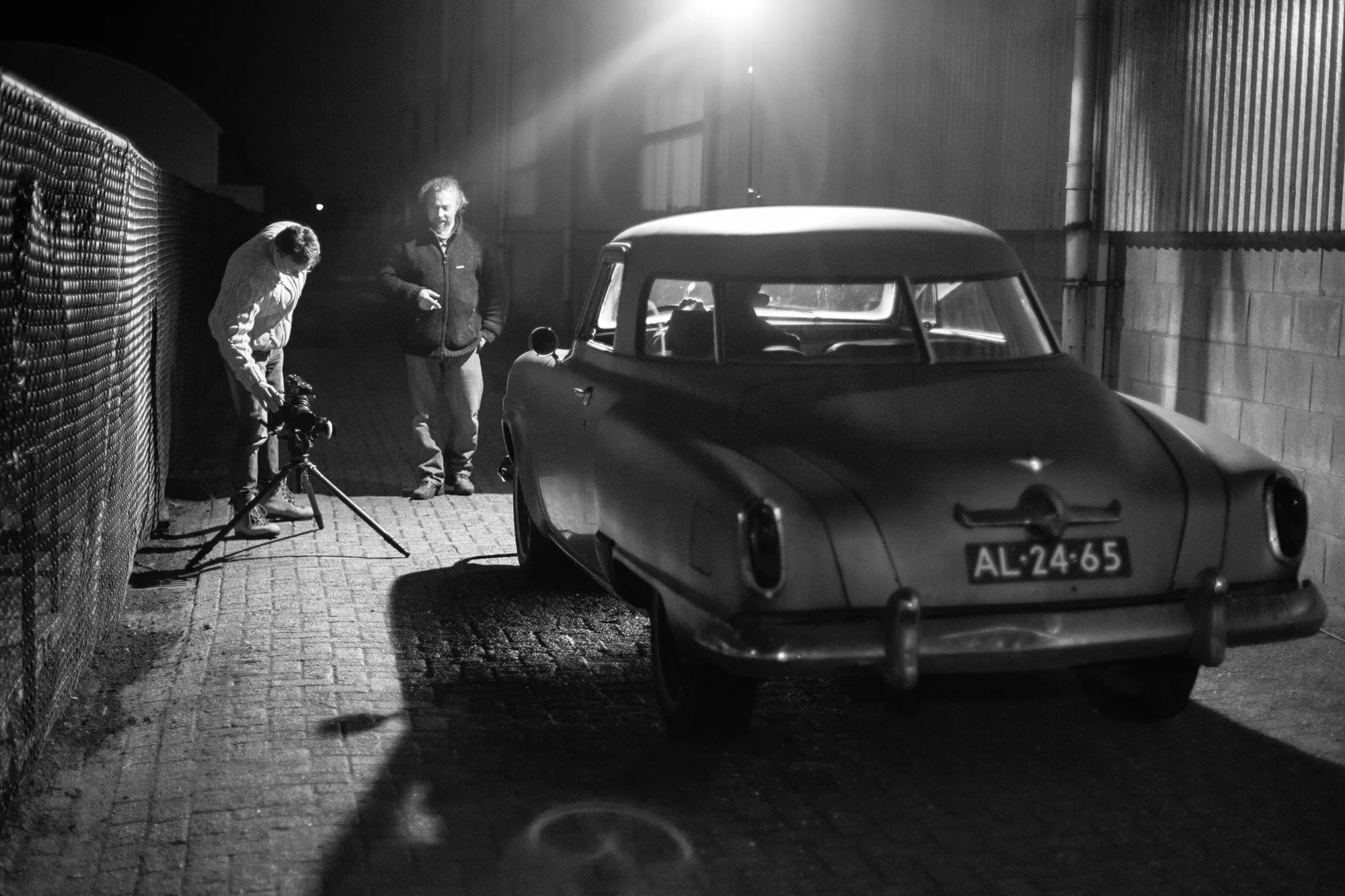 Zwart-wit foto nachts: vintage auto met personen bij hek