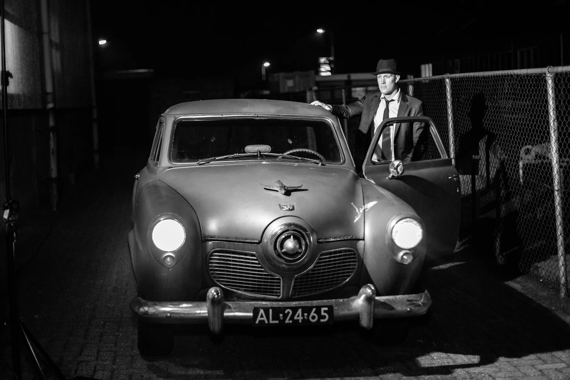 Man in suit and hat standing next to vintage car at night