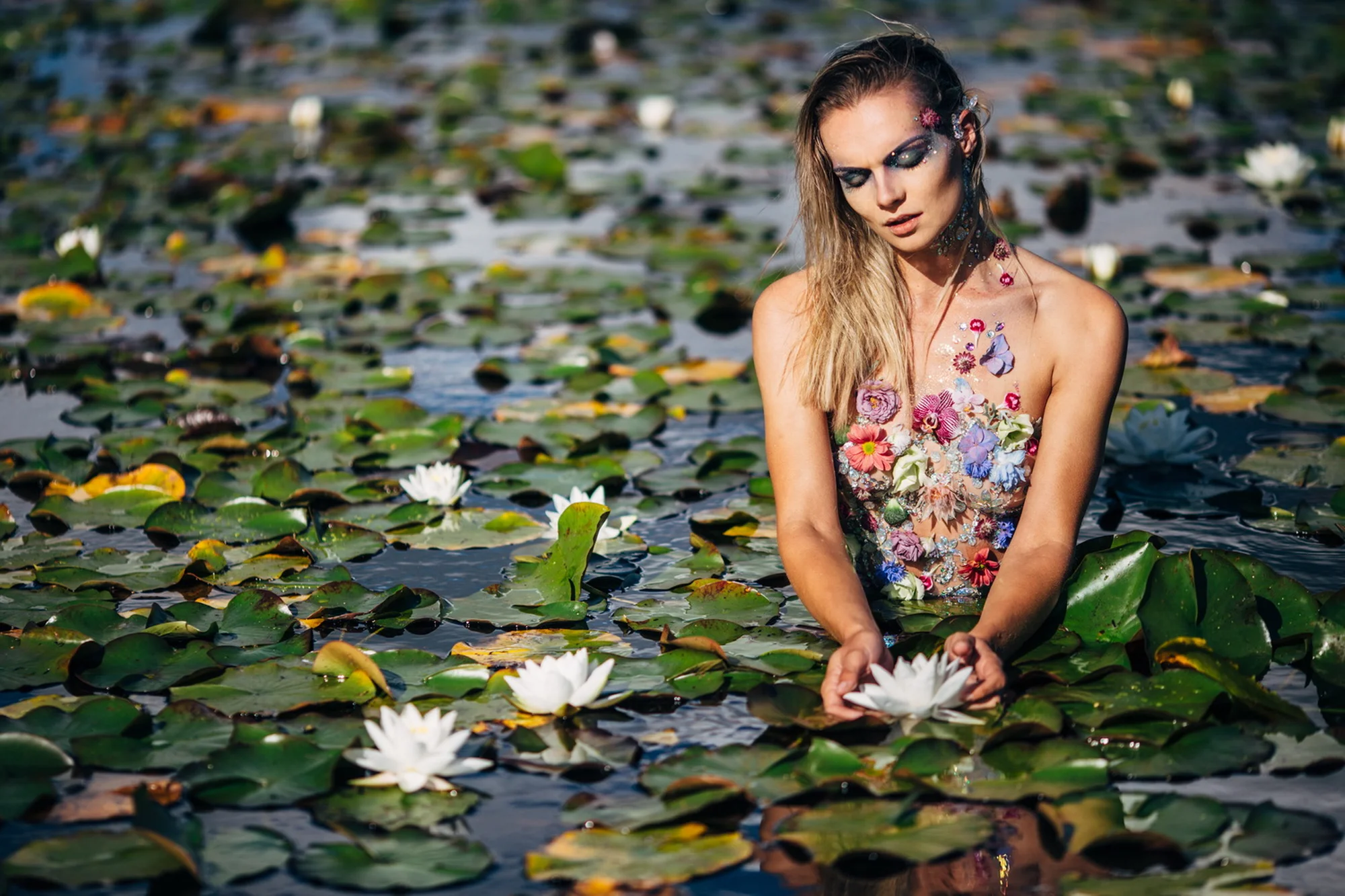 Vrouw in bloemenjurk zit tussen waterlelie's in vijver