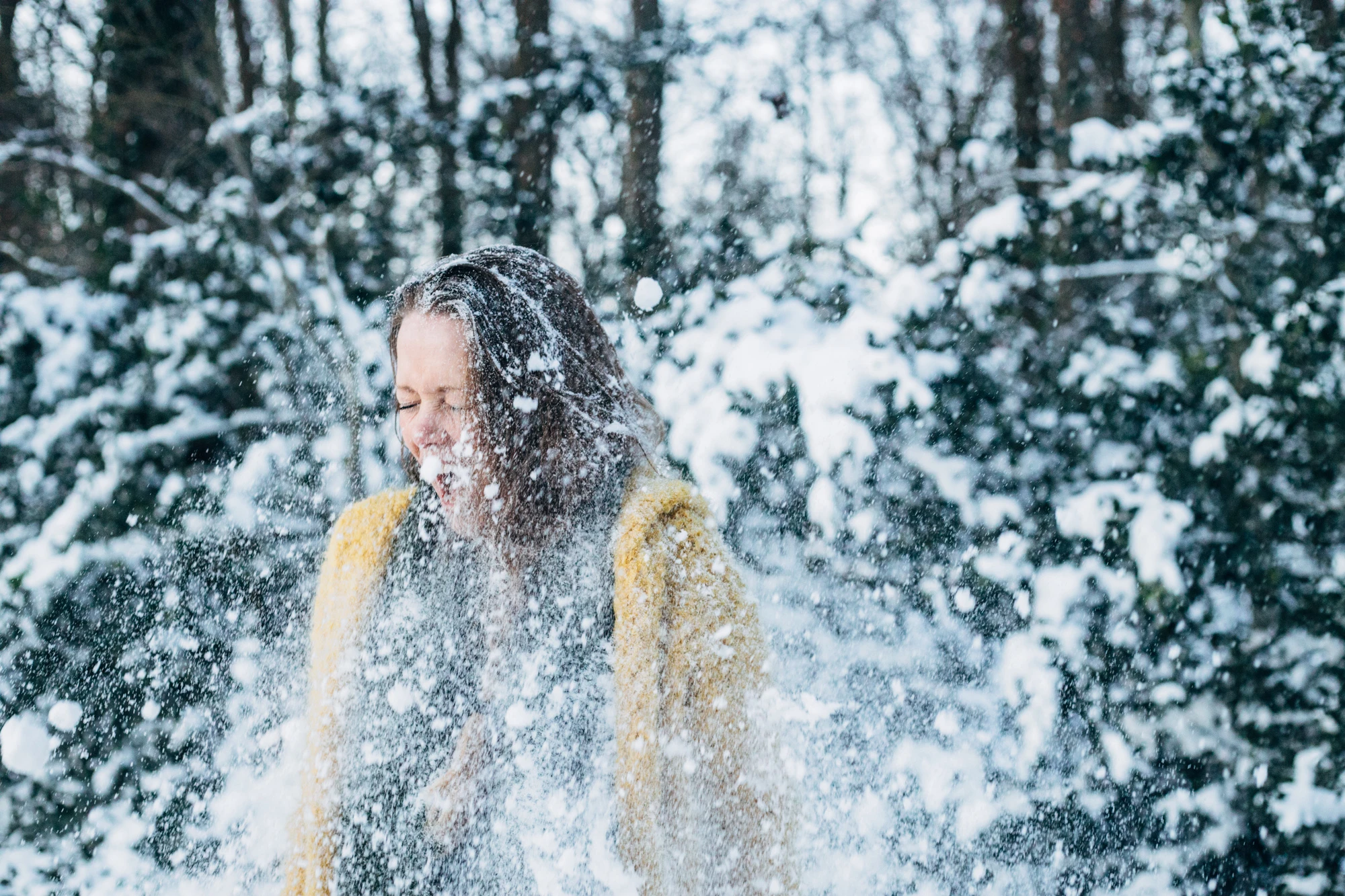 Meisje in gele jas geniet van sneeuwval in bos